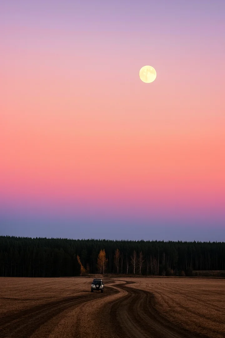 Luna piena nel cielo rosa al tramonto e veicolo su strada di campagna.