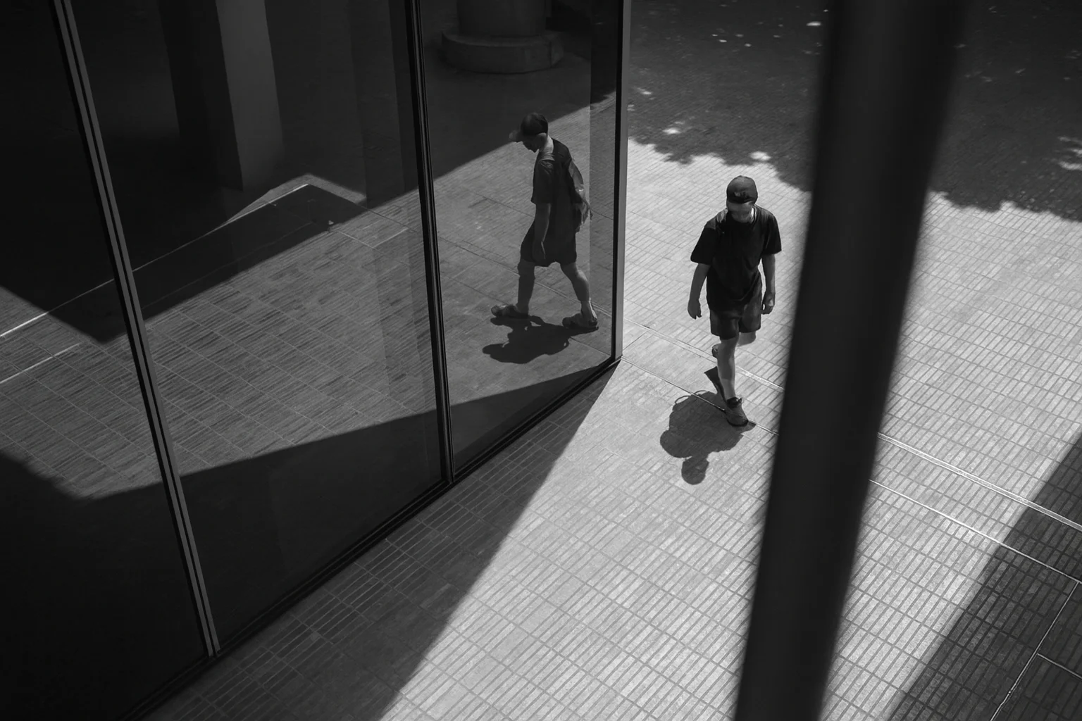 Pessoa caminhando e seu reflexo no vidro em preto e branco.