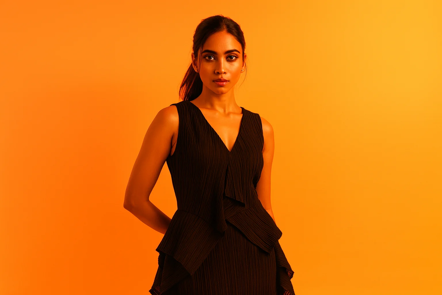 オレンジ背景の前に立つ黒いドレスの女性。