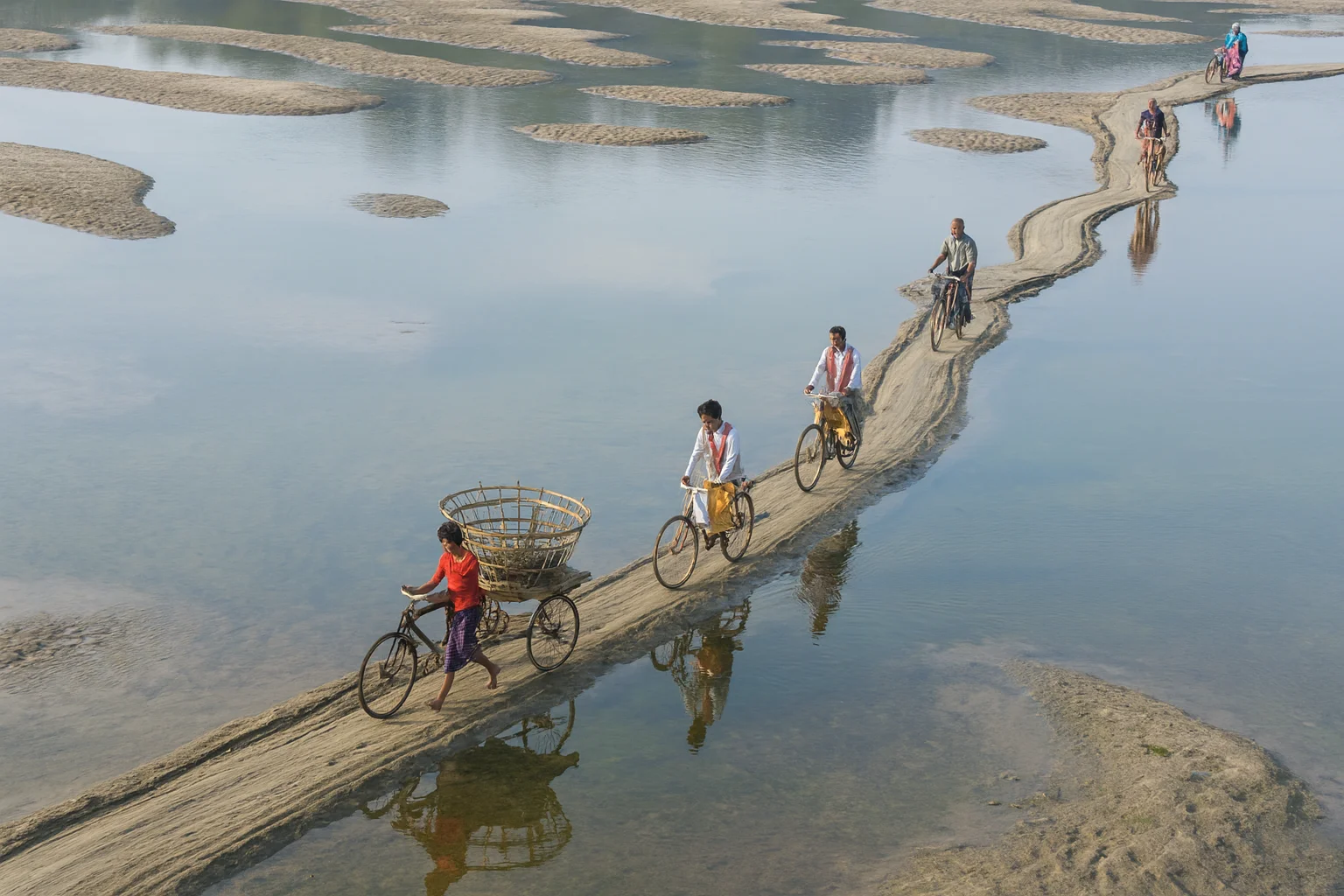 Persone che pedalano su un sentiero stretto sopra un fiume poco profondo